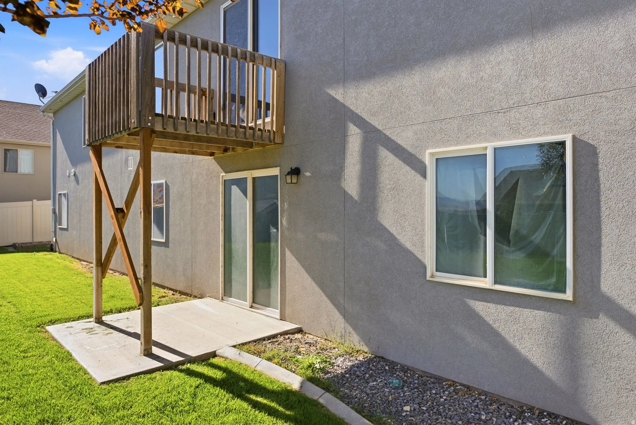 Stucco exterior with a ground-level concrete patio, sliding glass door access, and an elevated wood deck