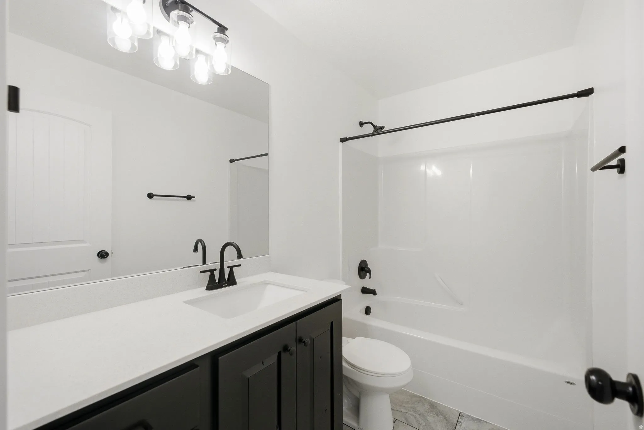 Bathroom featuring a dark wood-finish vanity with a white countertop, an integrated sink, a large wall-mounted mirror, and a shower/tub combination with dark fixtures