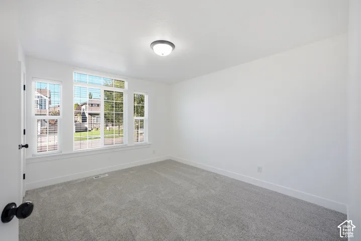 Recessed lighting, large window with blinds, light gray carpeting, white walls, and a white door with black hardware