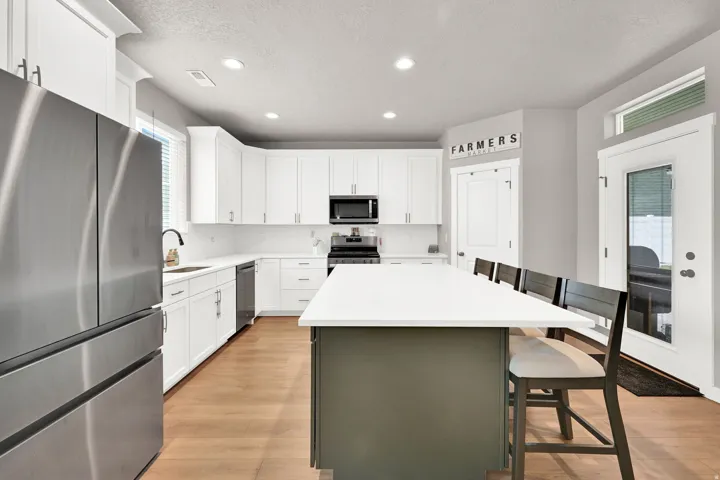 Kitchen featuring white cabinetry, stainless steel appliances, a center island with seating, wood-finish flooring, and recessed lighting
