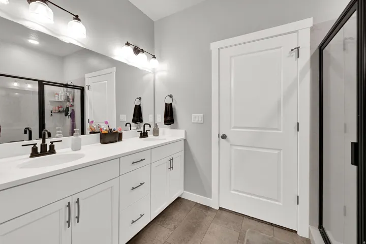 Double vanity with integrated sinks, white cabinetry, dark bronze fixtures, framed mirror, and tile flooring