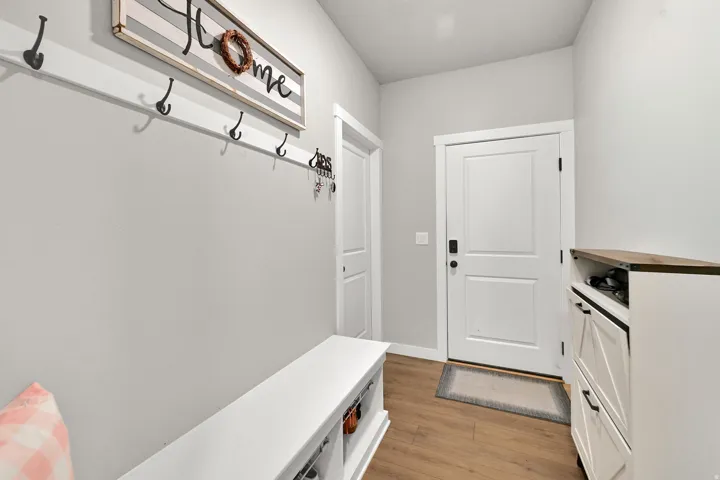 Wood-finish flooring, built-in coat rack, white paneled door, and built-in storage bench