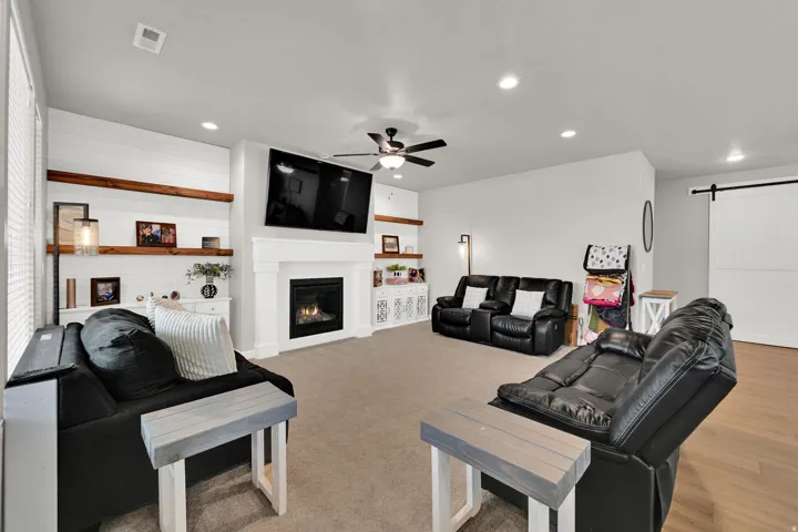 Carpeted living area featuring a fireplace with a white mantel, recessed lighting, ceiling fan, and built-in shelving with wood accents