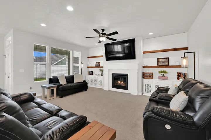 Living area featuring a fireplace with a mantel, built-in shelving with wood accents, recessed lighting, a ceiling fan, and large windows