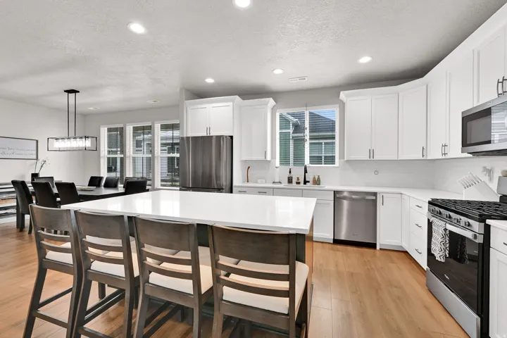 Kitchen featuring white cabinetry, stainless steel appliances, a large island with seating, wood-finish flooring, and recessed lighting