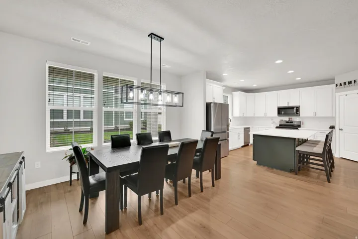 Open-concept living space with wood-finish flooring, a modern linear chandelier, and multiple windows