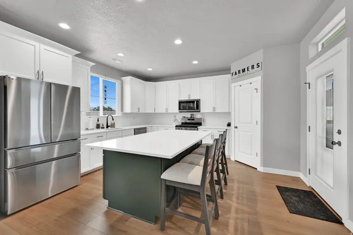 Kitchen featuring wood-finish flooring, white cabinetry, stainless steel appliances, a center island with countertop seating, and recessed lighting
