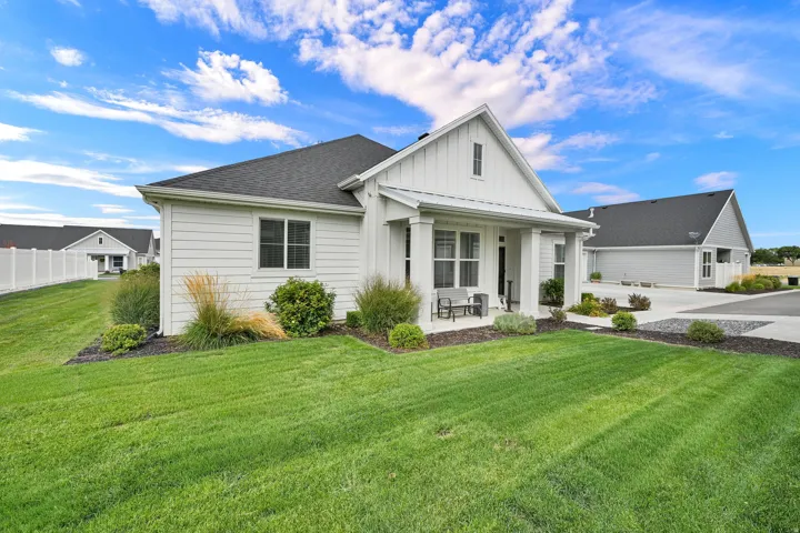 Contemporary farmhouse exterior with white siding, dark shingle roof, covered porch, and a lush lawn
