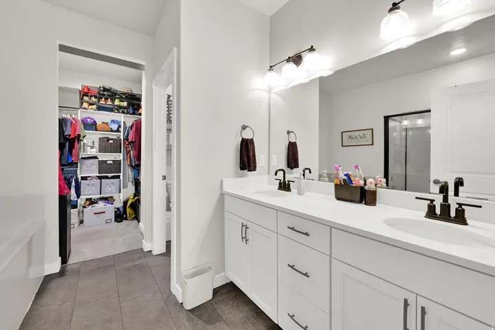Dual vanity with integrated sinks, white cabinetry, bronze fixtures, and a large mirror