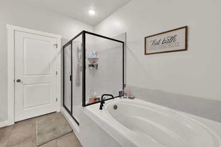 Soaking tub with matte black fixtures, walk-in shower with black-framed glass enclosure, and recessed lighting