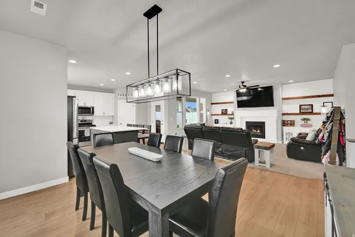 Open-concept living space with wood-finish flooring, a contemporary linear chandelier, a fireplace with a mantel, built-in shelving, and recessed lighting