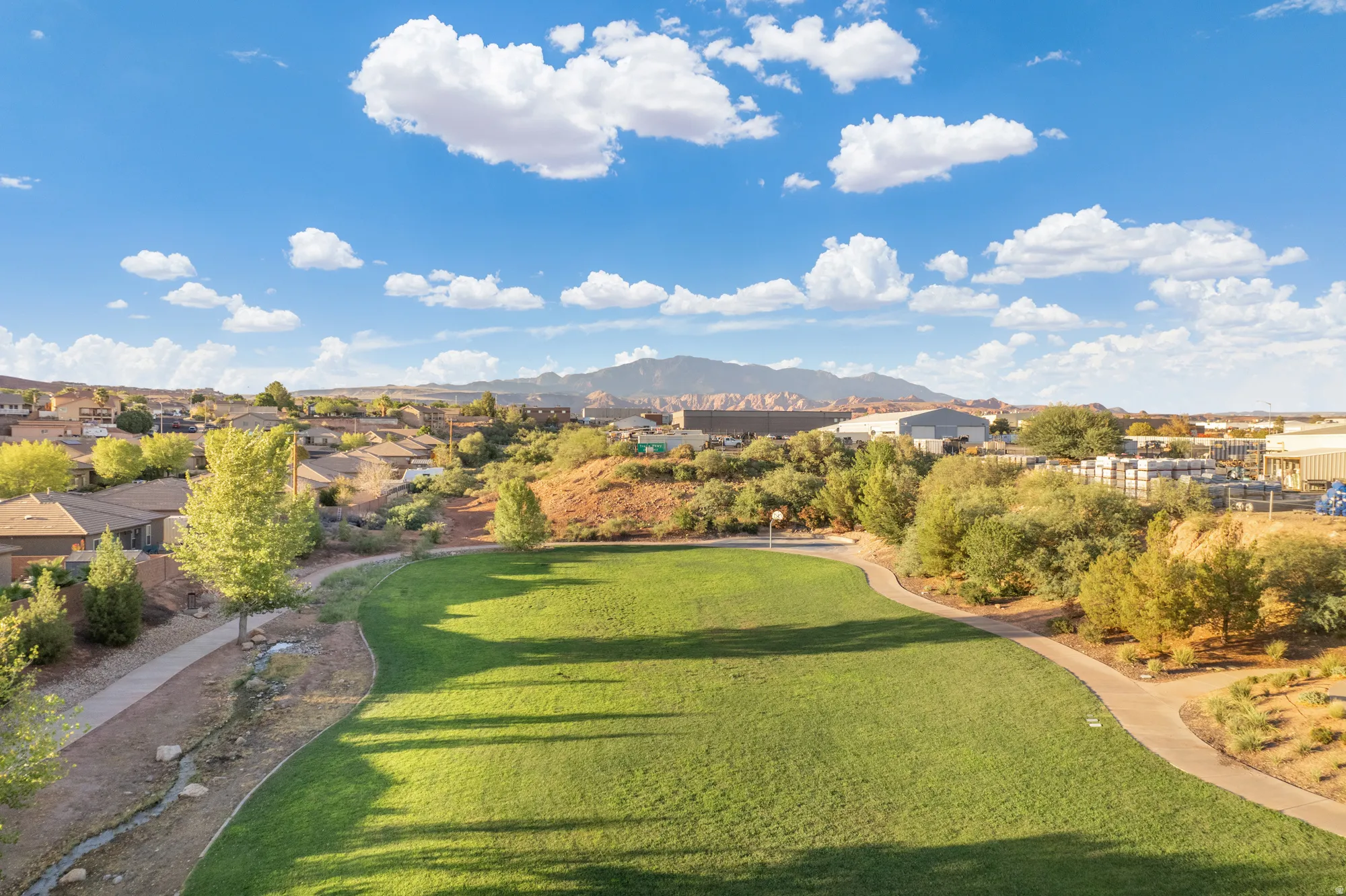 Expansive green space featuring a walking path, surrounding residential homes, and distant mountain scenery
