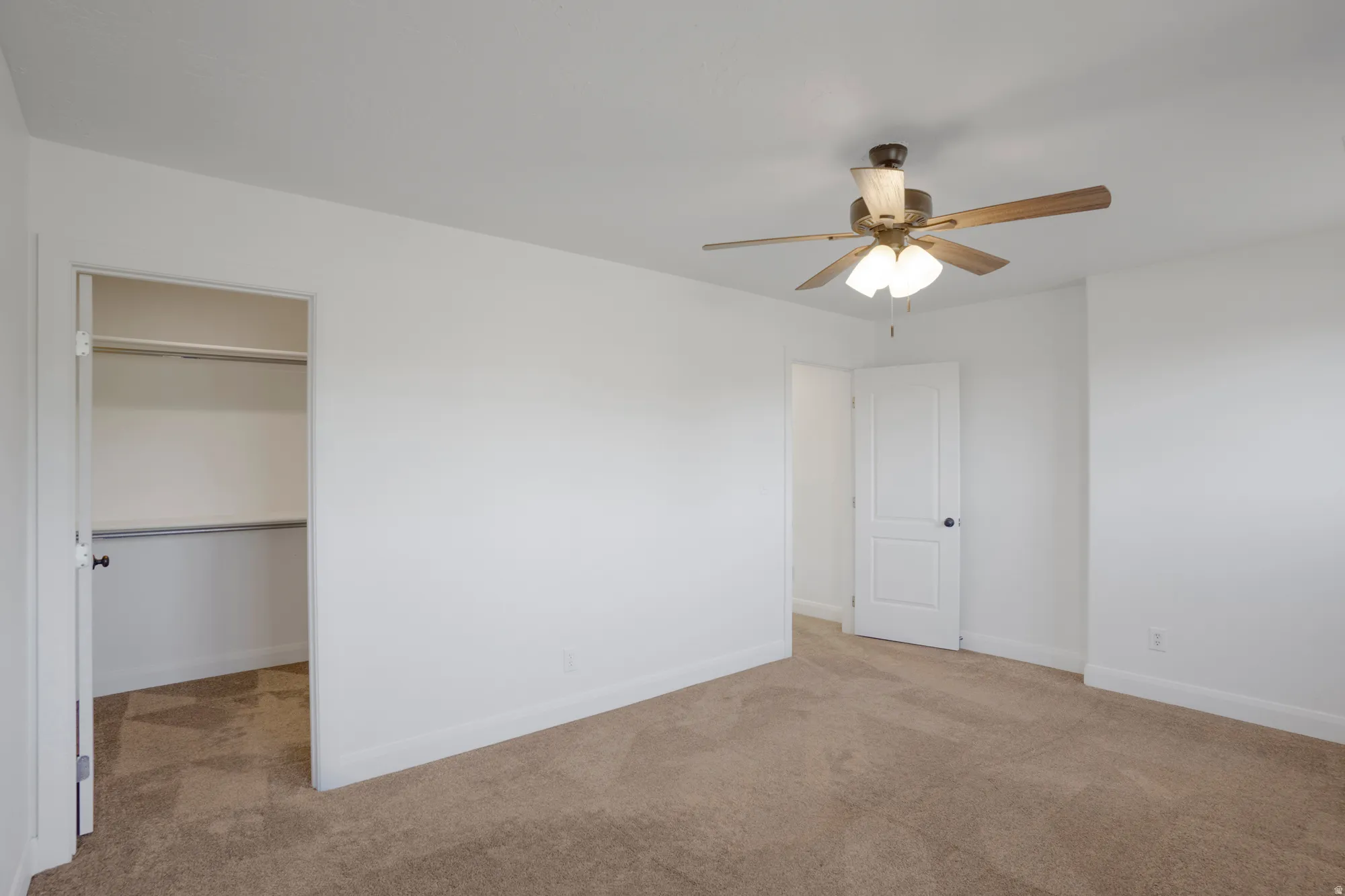 Plush carpeted flooring, a ceiling fan with integrated lighting, a built-in closet with shelving and hanging rod, and white painted walls