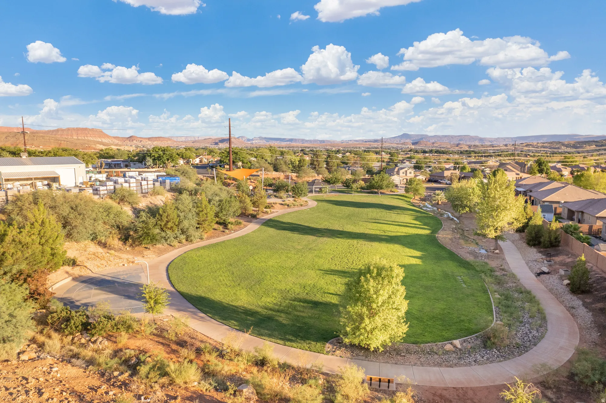 Expansive green space featuring a walking path, mature trees, and red rock landscape backdrop