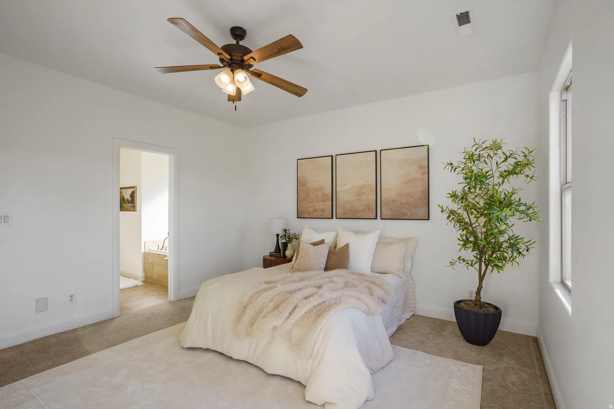 Carpeted flooring, ceiling fan with integrated lighting, natural light through a window, and an open doorway to a bathroom with a built-in tub