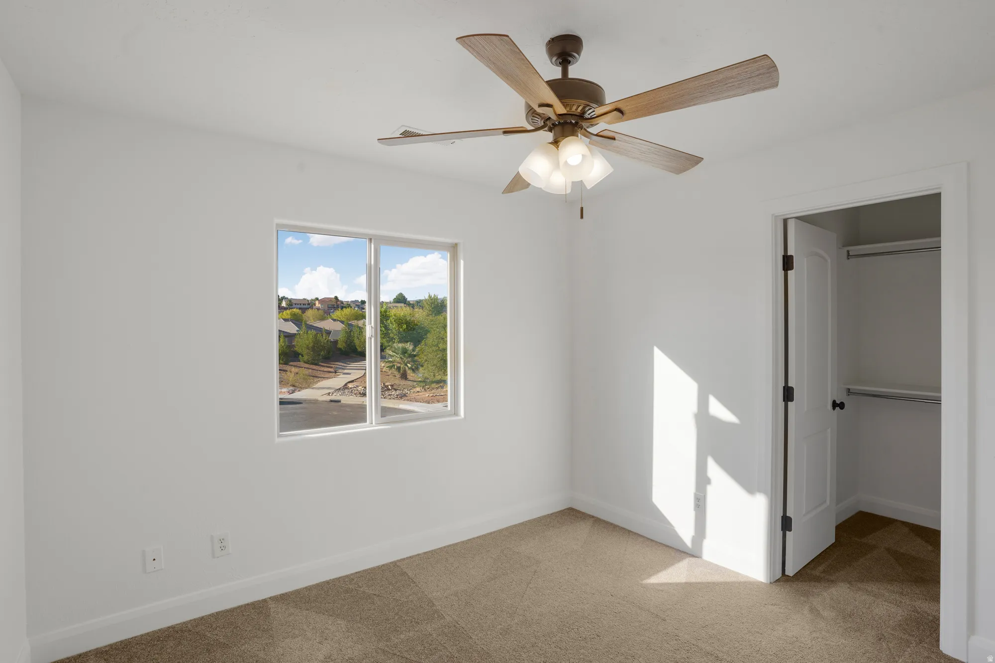 Recessed window framing exterior scenery, ceiling fan with integrated lighting, built-in closet with shelving and hanging rod, light-toned carpeting, and crisp white walls