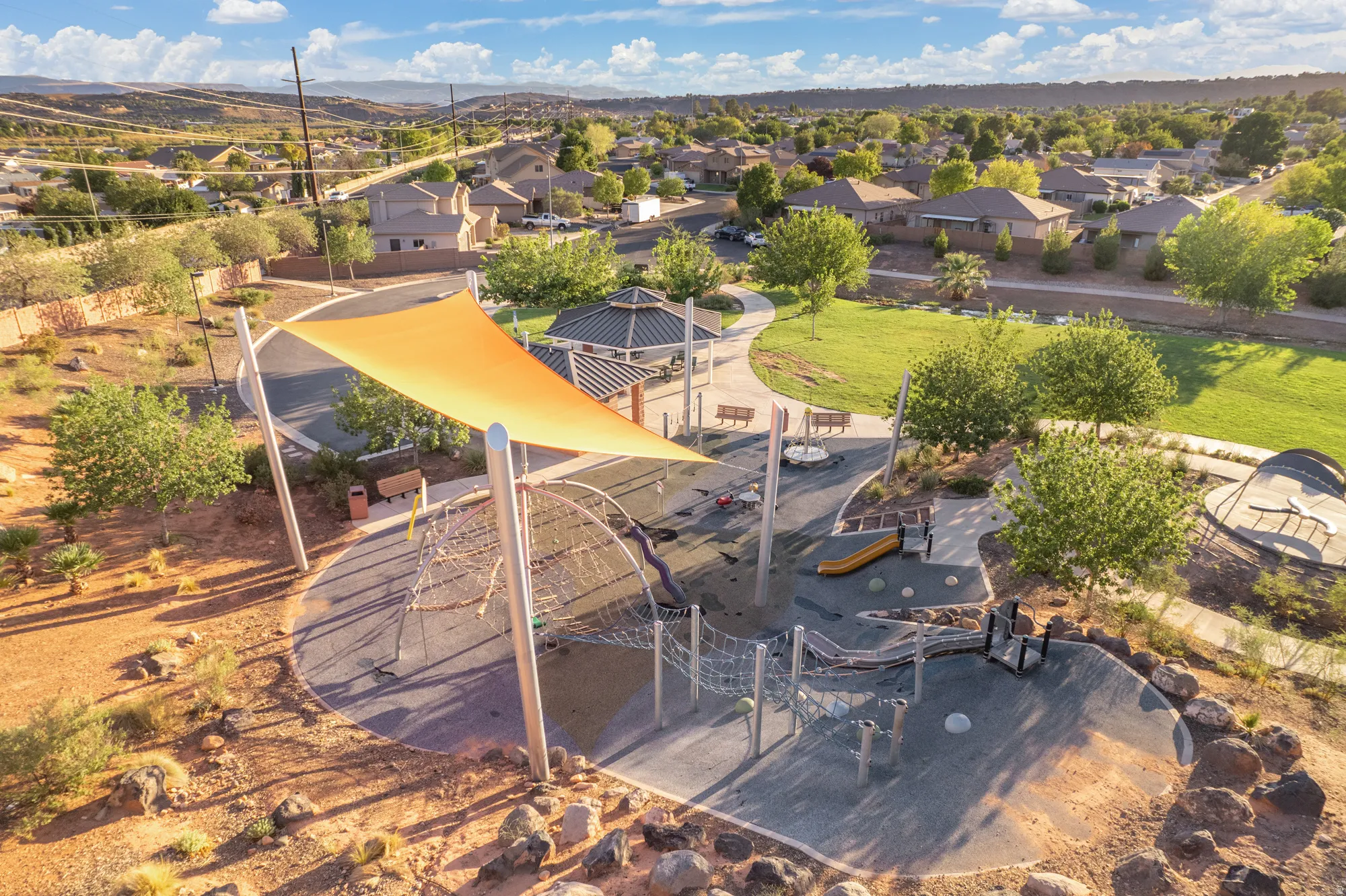 Community park with a playground featuring shade structures, a gazebo, paved pathways, and grassy areas