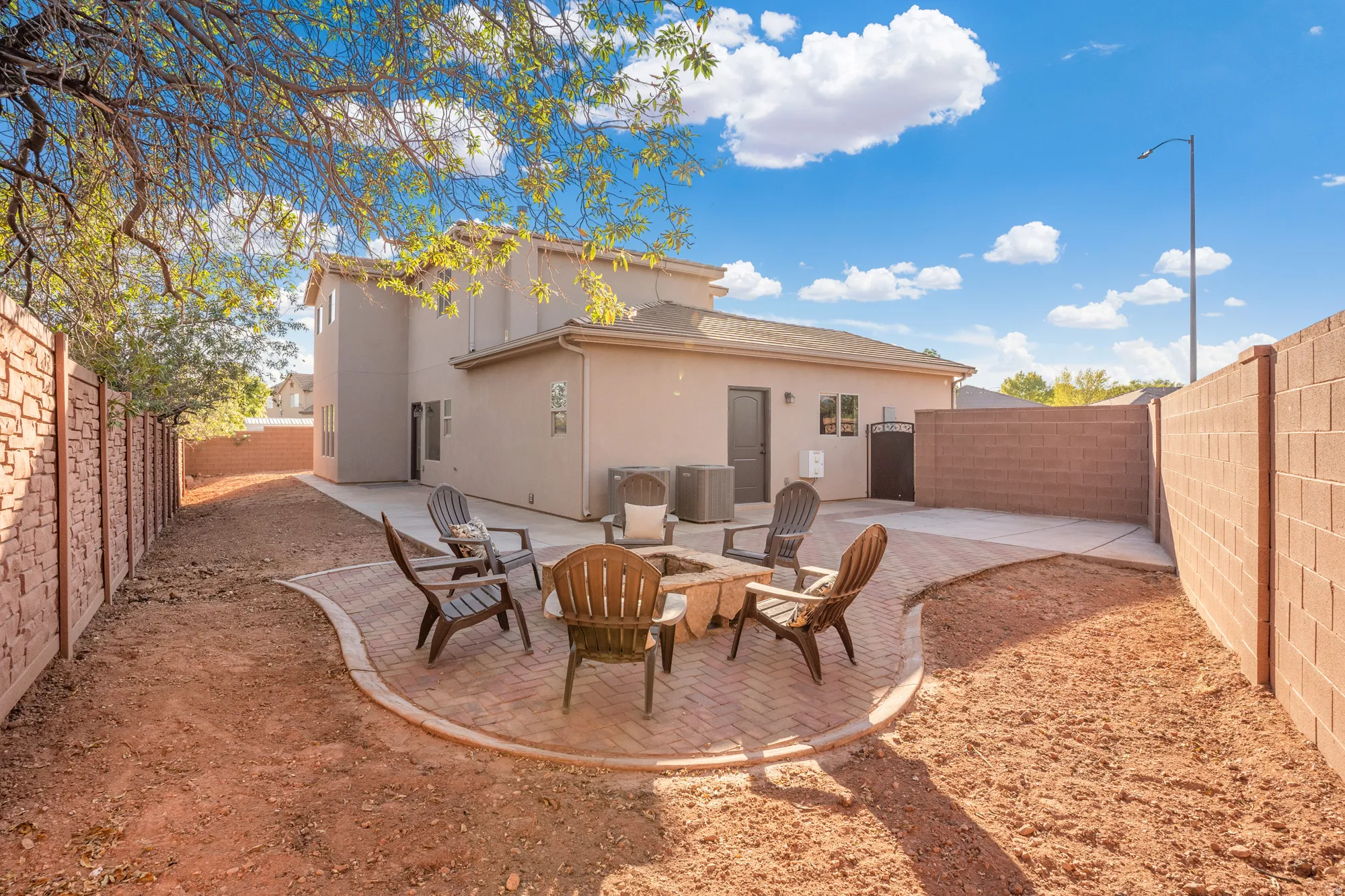 Expansive backyard featuring a curved brick paver patio, partial block wall fencing, and a concrete slab area