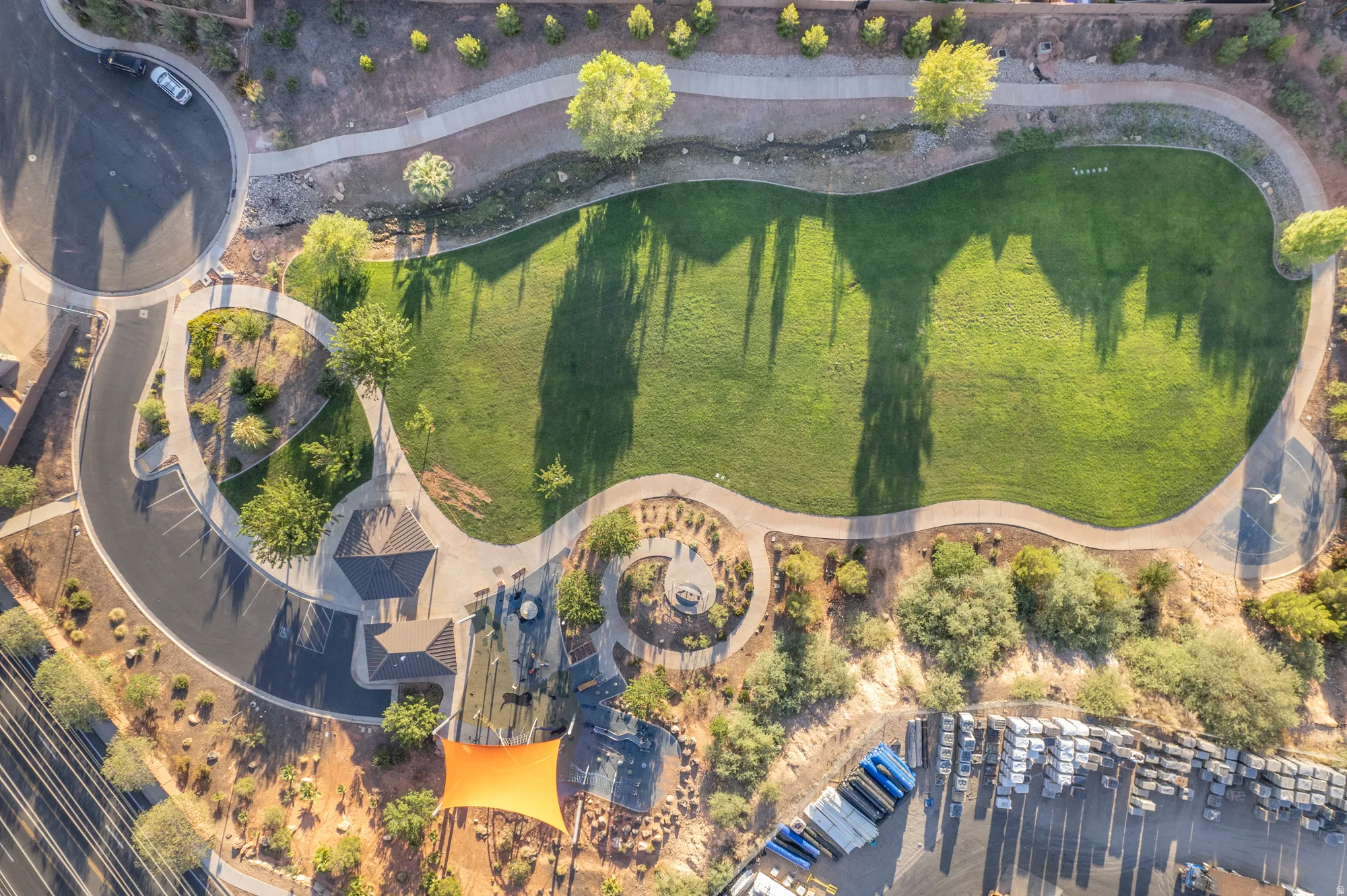Expansive manicured lawn with mature specimen trees and defined landscape beds, anchored by a circular hardscape feature and winding paved pathways