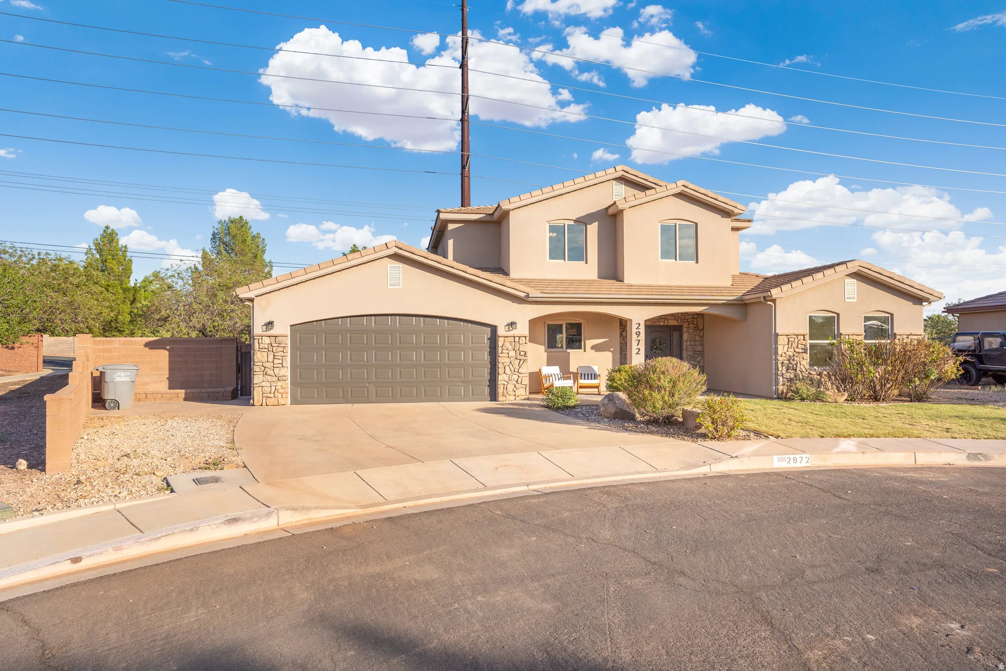 Stucco exterior with stone accents, arched garage door, covered front entry, concrete driveway, and front landscaping