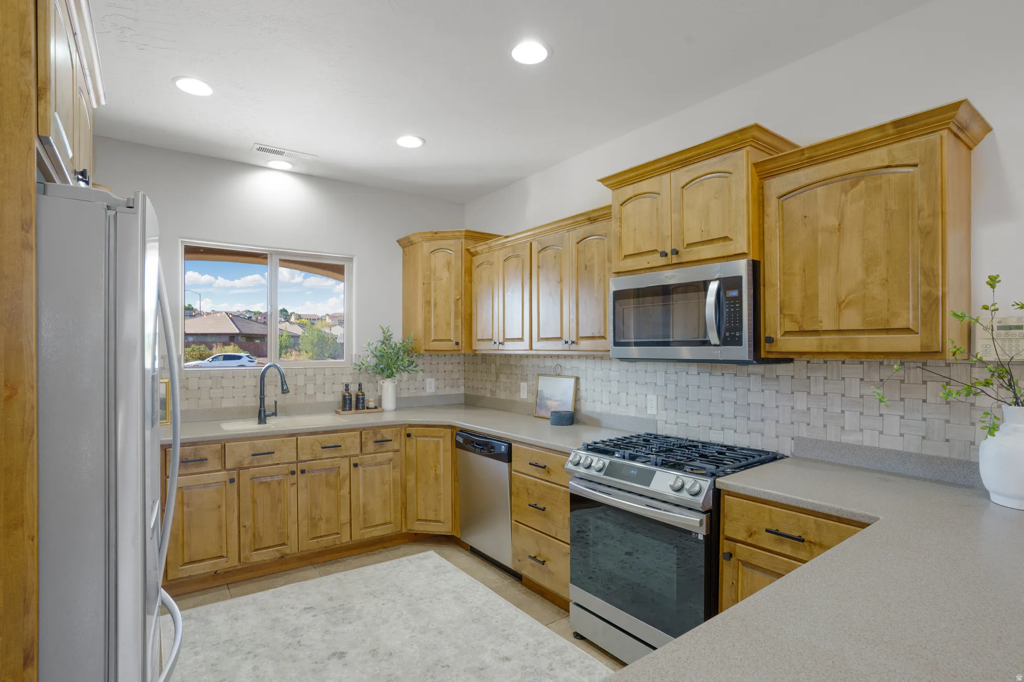 Kitchen with recessed lighting, light wood-finish cabinetry, stainless steel appliances, a window, and a tile backsplash