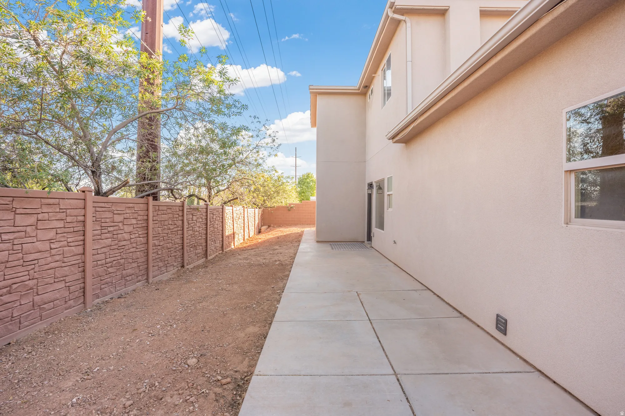 Stucco exterior with multiple windows, concrete walkway, and a textured privacy fence