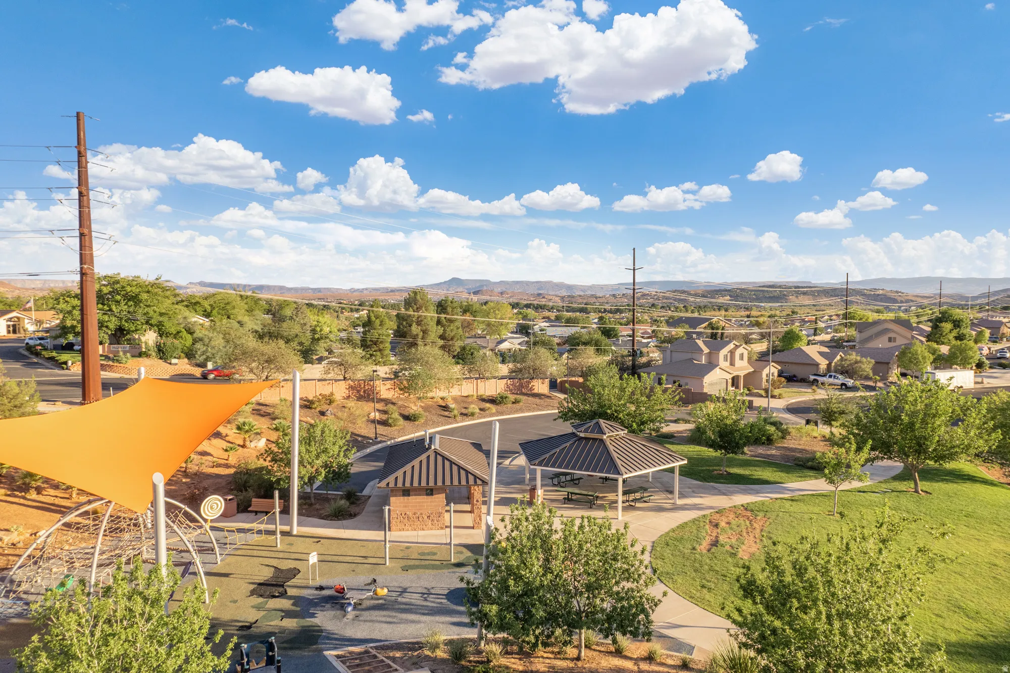 Community park featuring a playground with a sun shade, multiple covered picnic areas, walking paths, and expansive green spaces