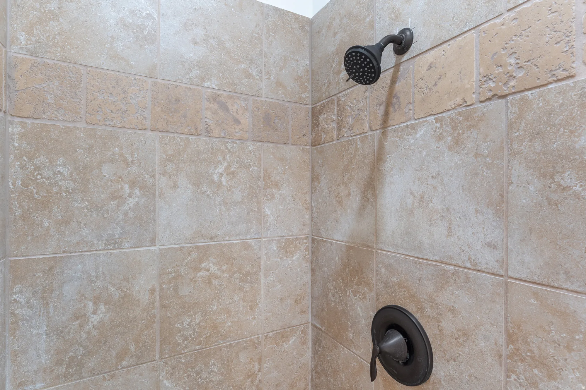 Shower with textured tile walls, decorative tile accent band, and an oil-rubbed bronze shower head and control