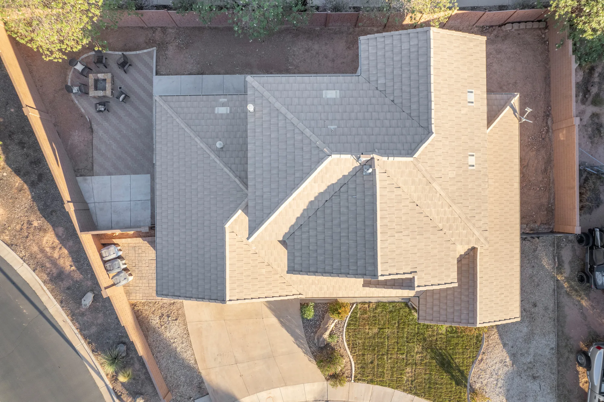 Asphalt shingle roof, paved patio with fire pit, concrete walkway, and landscaped front yard
