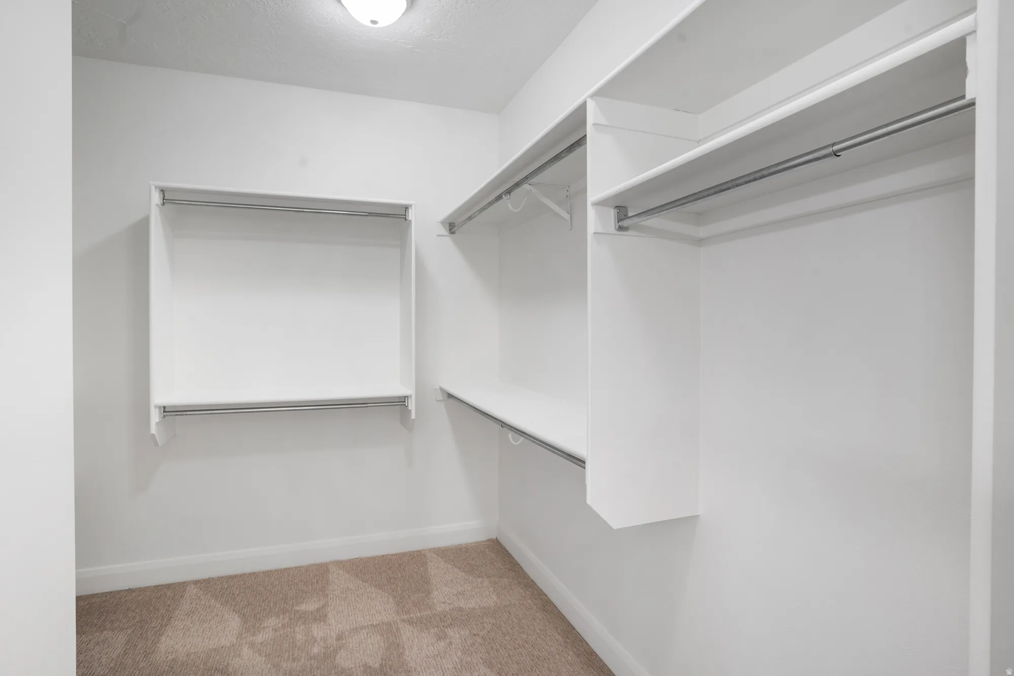 Walk-in closet with carpet flooring, white shelving, and multiple hanging rods