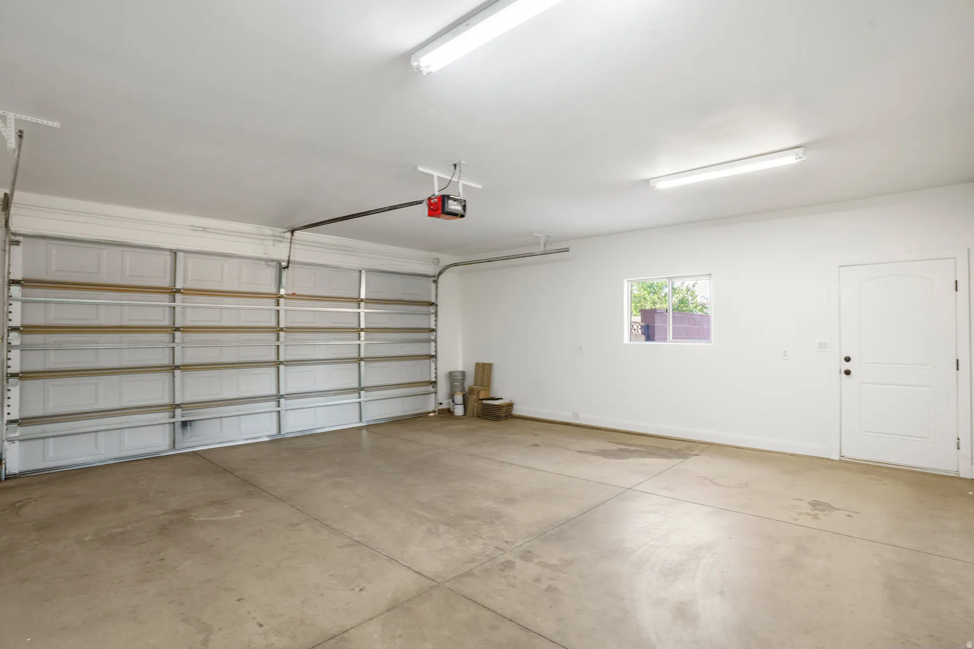 Spacious garage with a sectional overhead door, automatic opener, concrete flooring, and a white paneled door