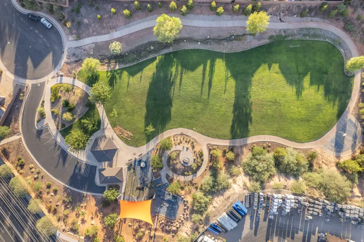 Expansive manicured lawn with mature specimen trees and defined landscape beds, anchored by a circular hardscape feature and winding paved pathways