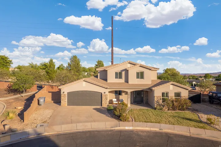 Two-story residence featuring a stucco exterior, stone facade accents, an attached two-car garage, covered front entry, and a paved driveway