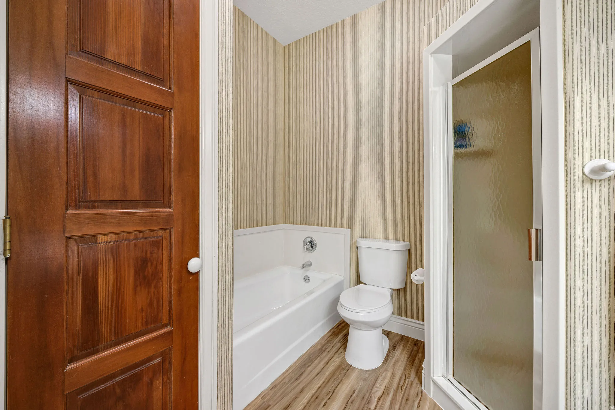 Wood-finish flooring, full-size bathtub, toilet, and shower enclosure with frosted glass