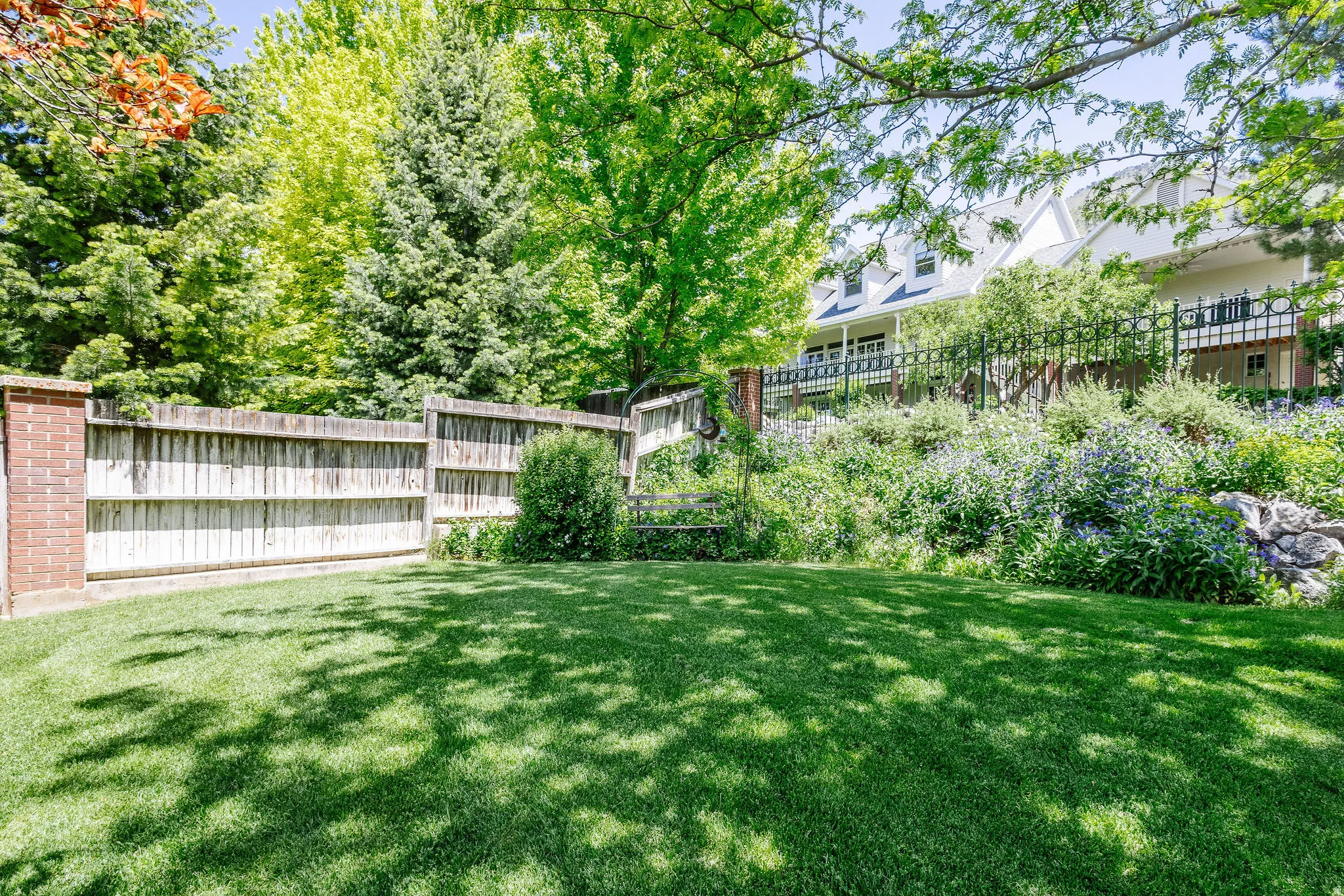 Expansive green lawn with a wood fence boundary, brick pillar accent, and mature trees