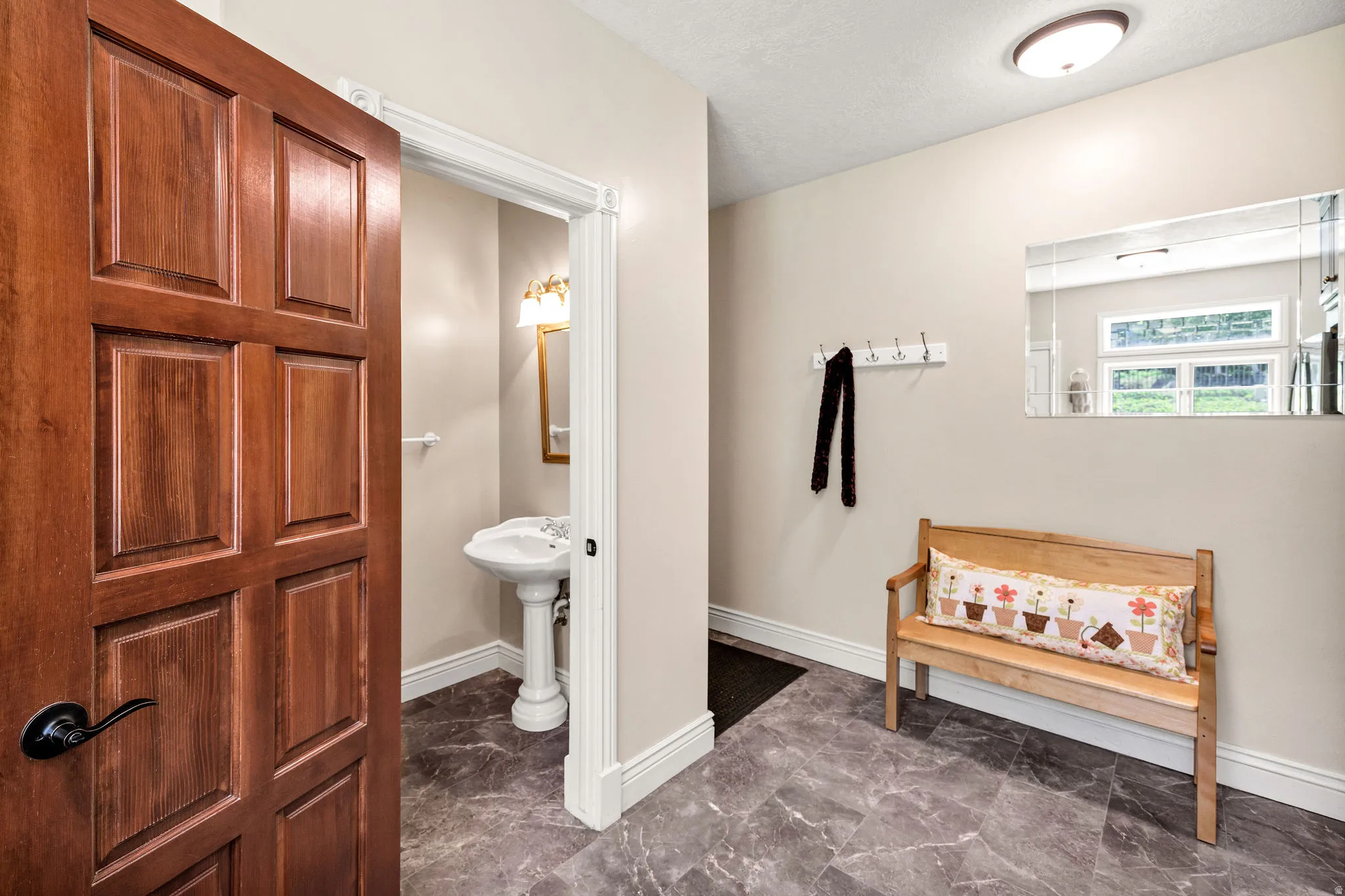Wood-paneled door with black hardware, leading to a space featuring a pedestal sink, wall-mounted sconce, and a mirror