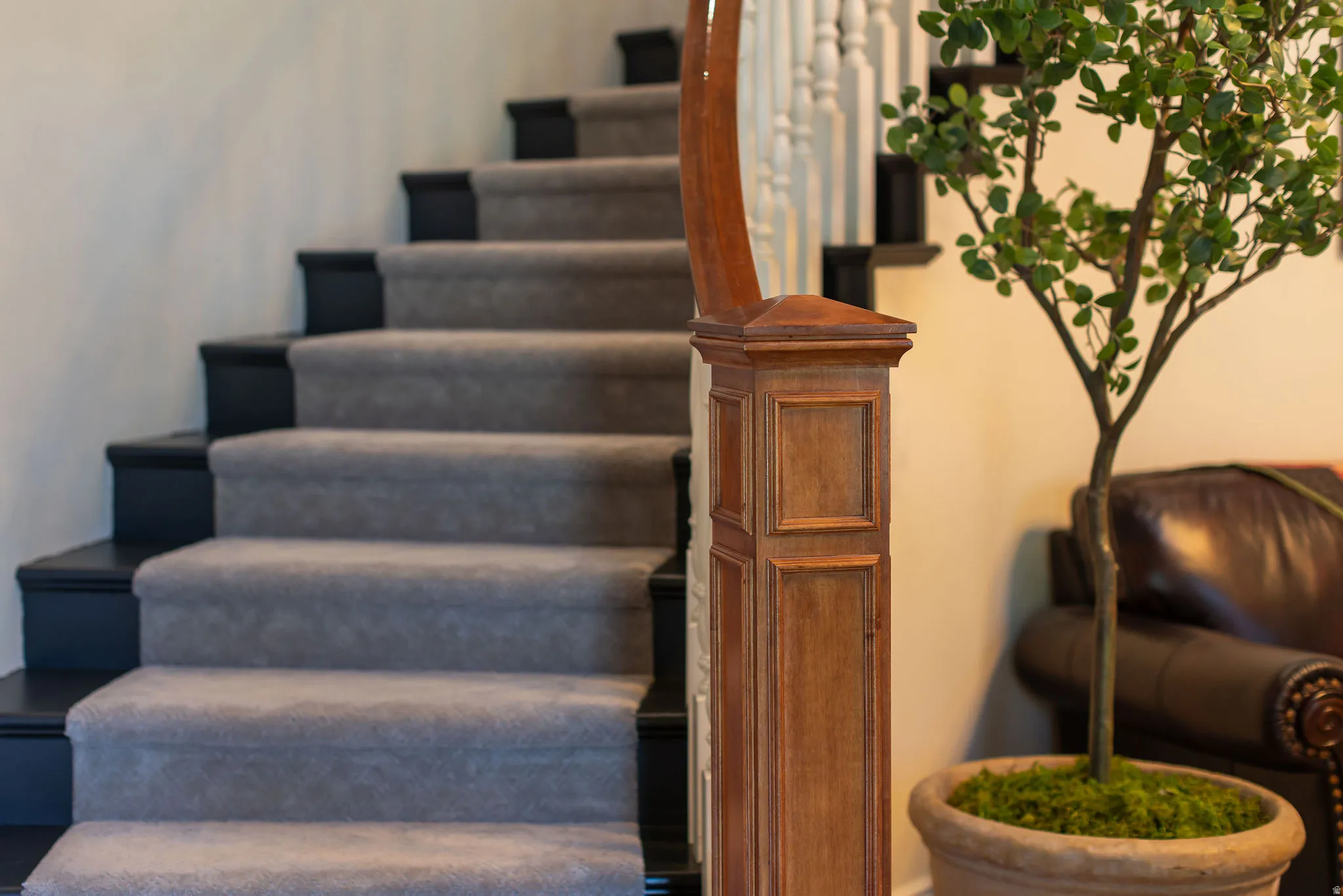 Staircase featuring light gray carpeting, dark risers, and a prominent wood newel post with panel detailing
