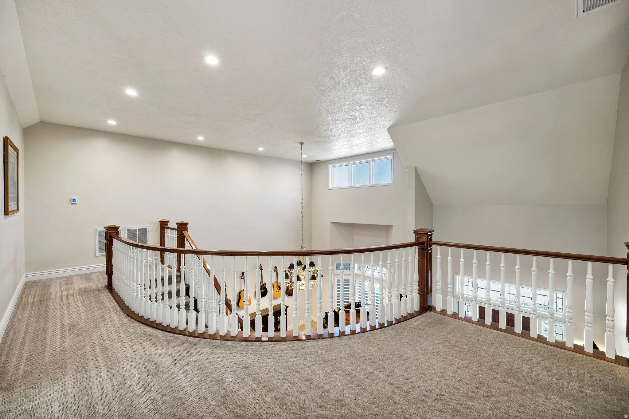 Carpeted loft space with a curved wooden banister and white spindles, recessed lighting, and a high ceiling