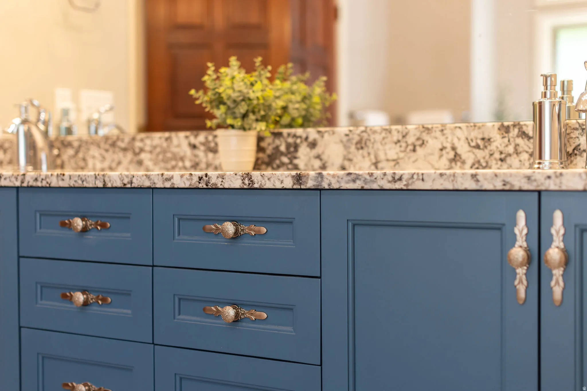Vanity featuring blue cabinetry, patterned countertop, and decorative bronze hardware