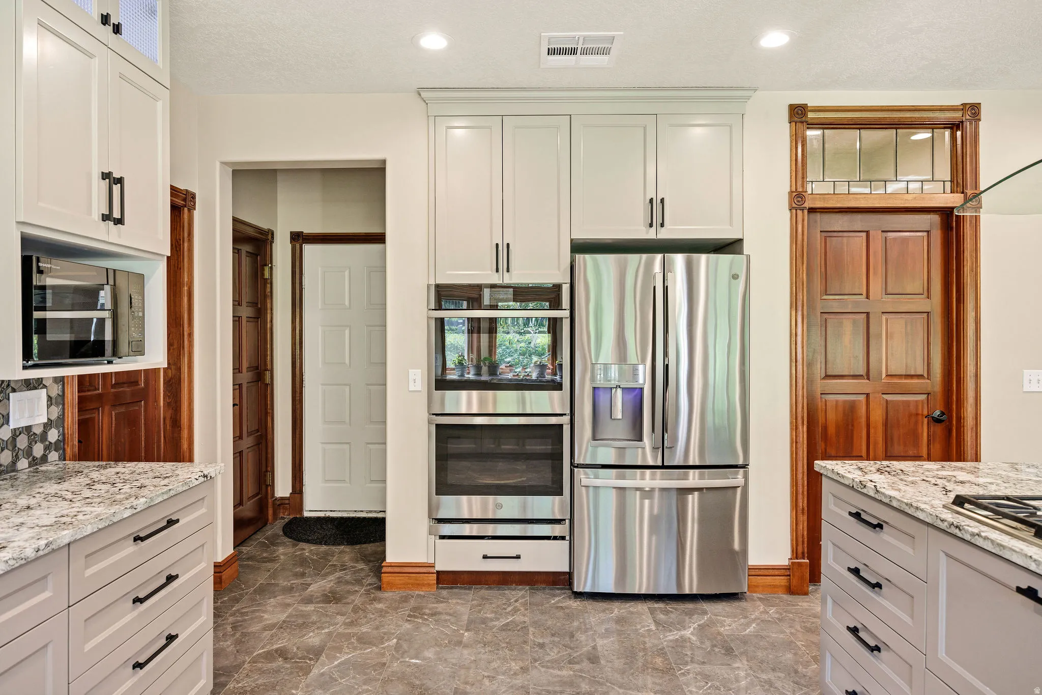 Kitchen featuring stainless steel appliances, built-in double oven, refrigerator, wood-finish base trim, and a decorative wood-frame transom window