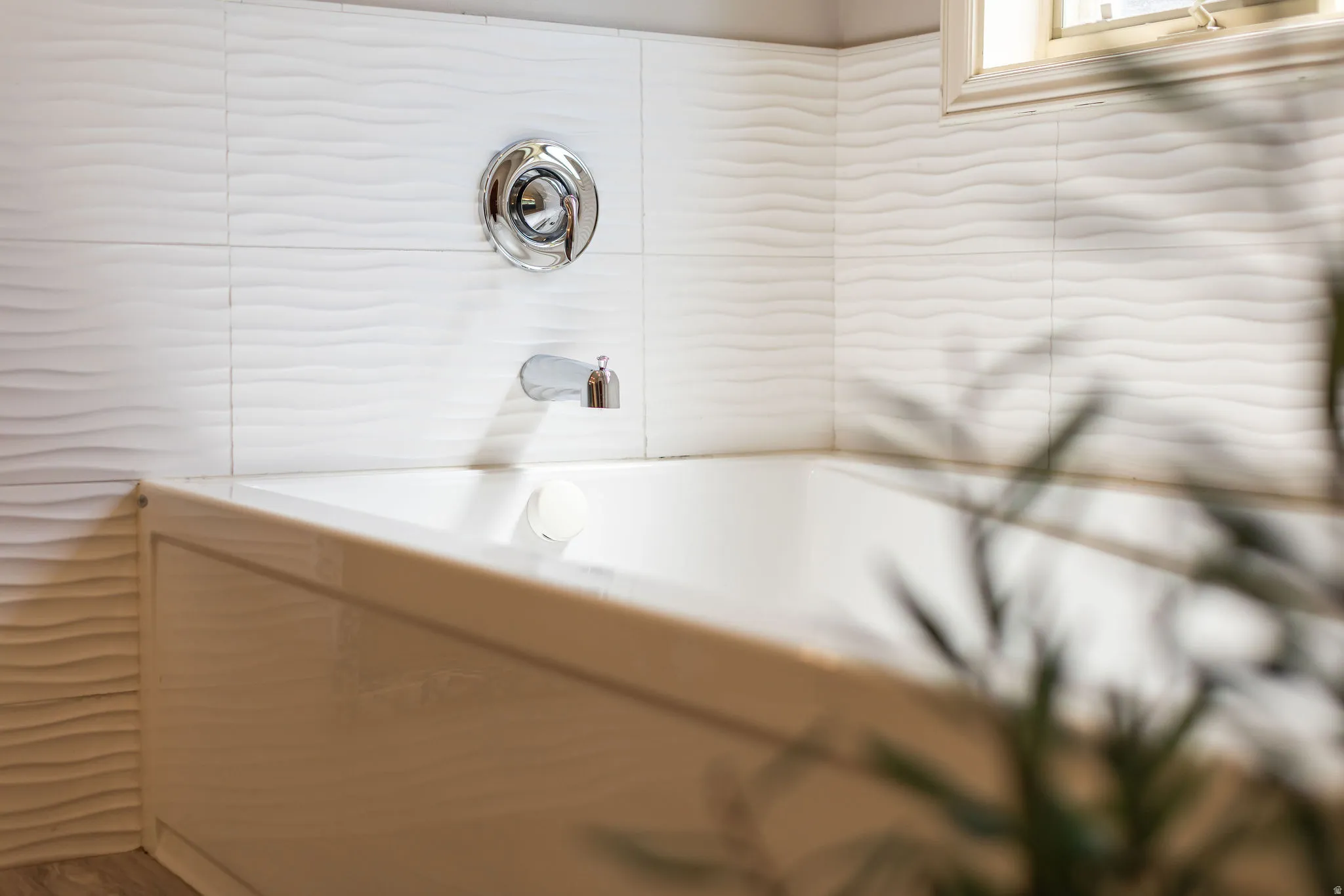 Recessed alcove bathtub with white finish, chrome fixtures, and textured wave-patterned wall tile