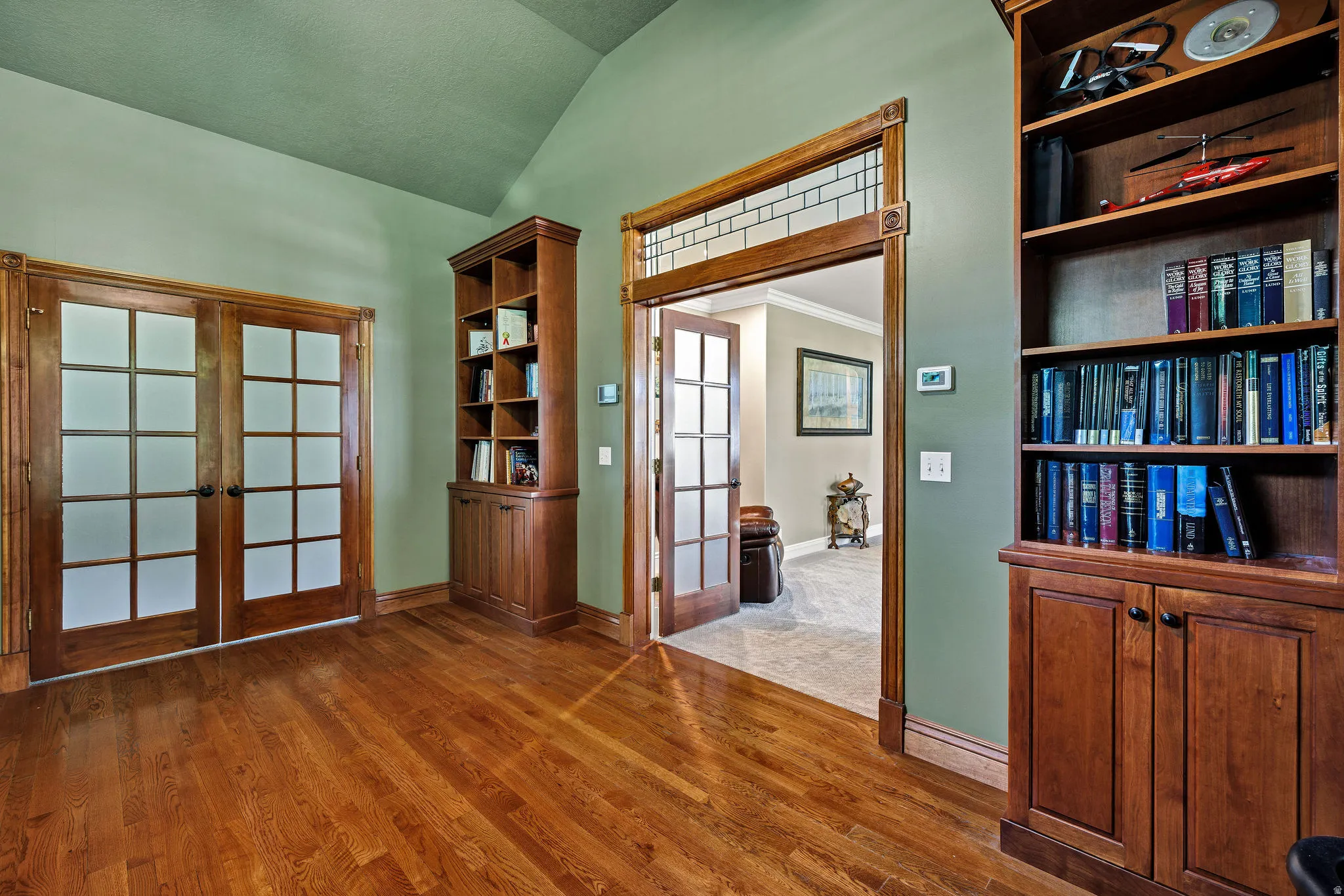 Hardwood flooring, wood-framed French doors, built-in wood cabinetry, vaulted ceiling, and decorative transom window