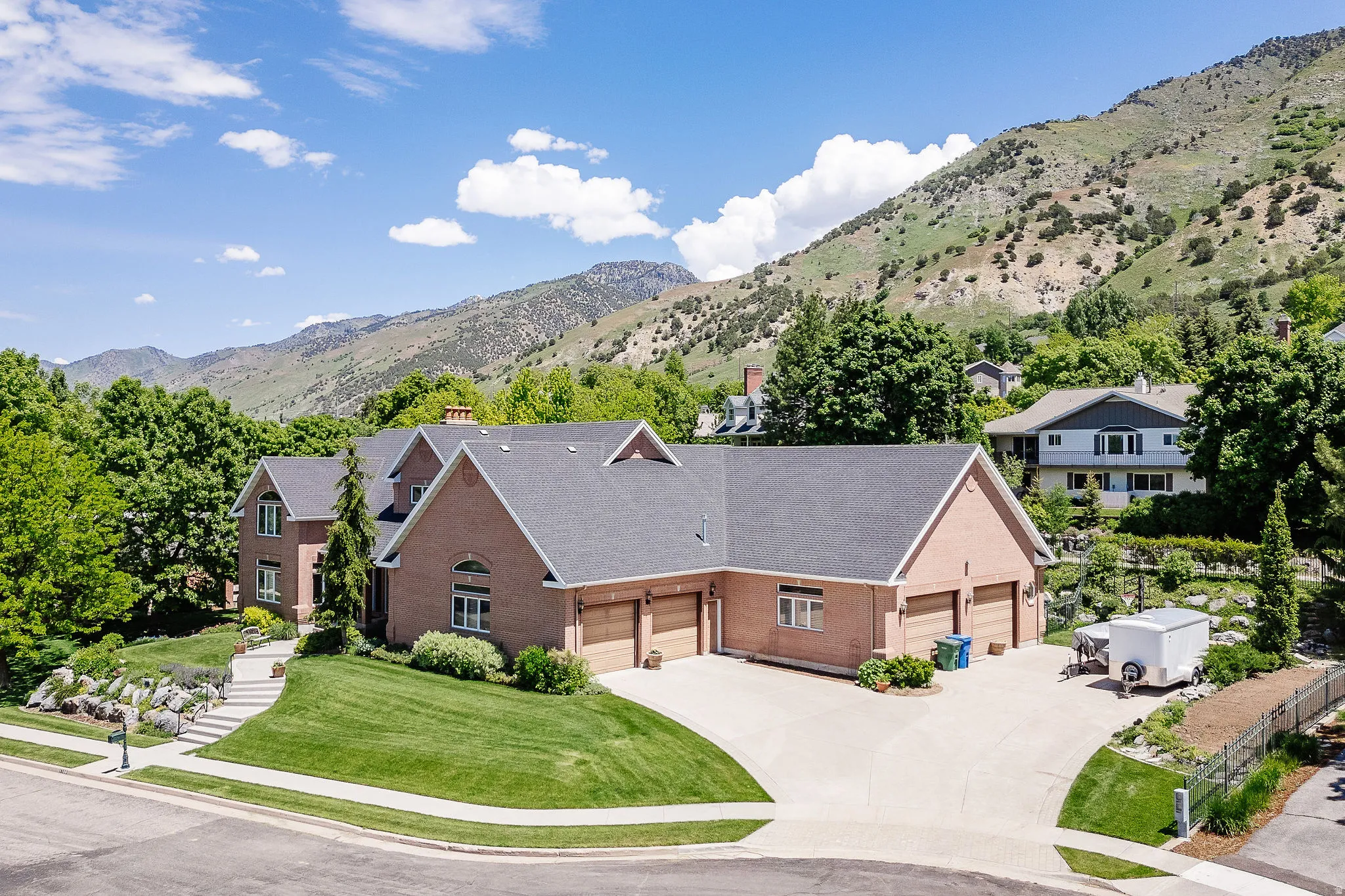 Brick exterior residence with a multi-car garage, mature landscaping, paved driveway, and mountain scenery