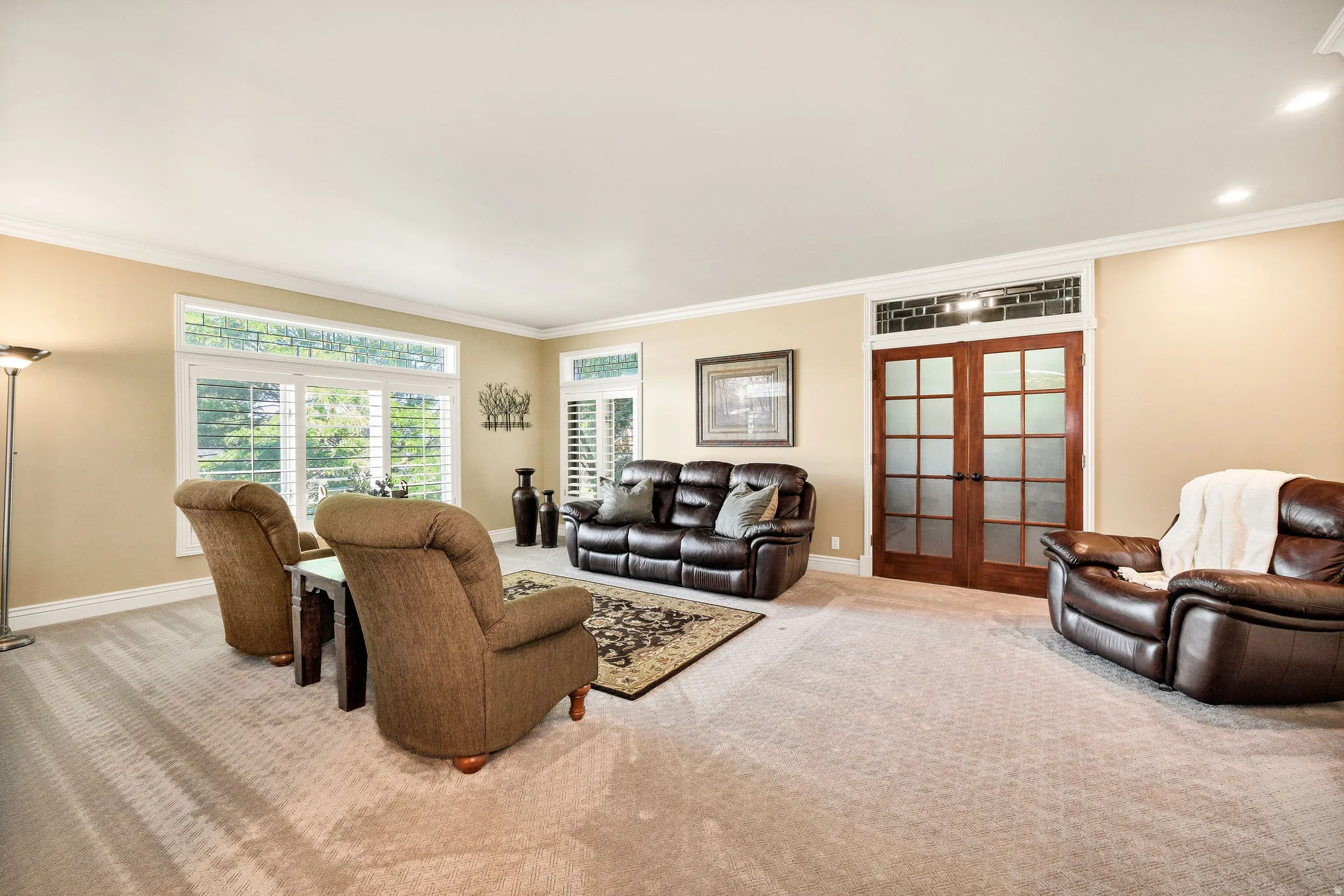 Recessed lighting, wood-frame double doors with frosted glass panels, transom window with intricate detailing, large windows with plantation shutters, and crown molding