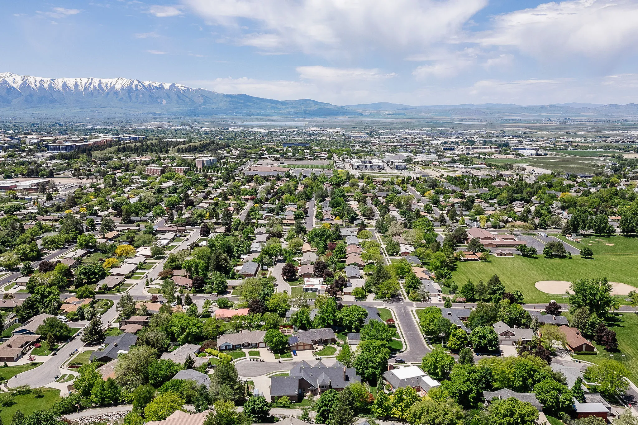 Established residential area with tree-lined streets, a prominent baseball field, and a distant mountain range featuring snow-capped peaks