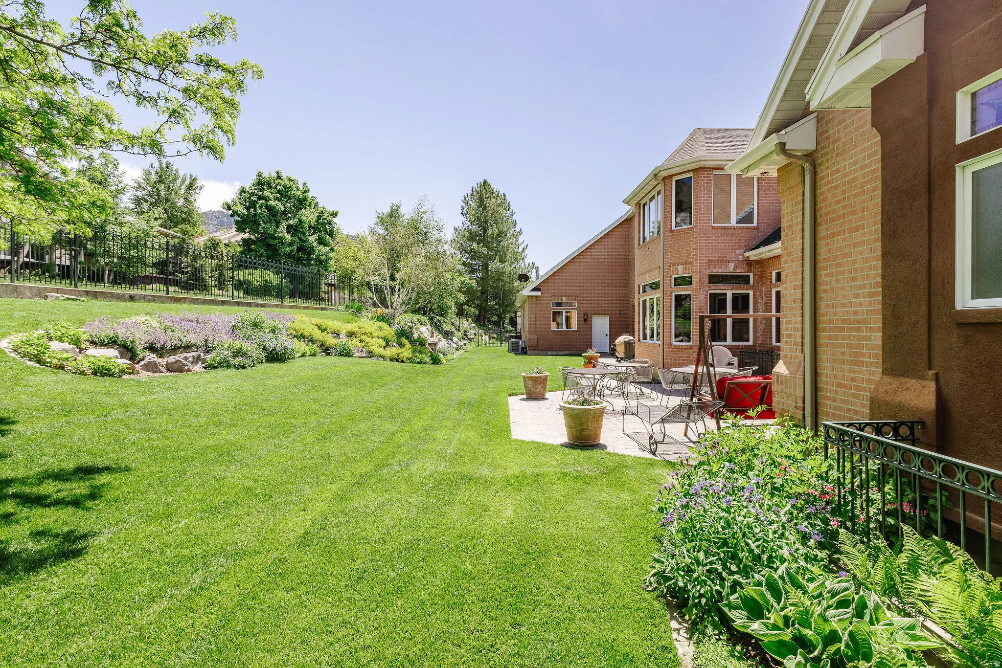 Expansive green lawn, established landscaping, paver patio, brick exterior, and multiple windows