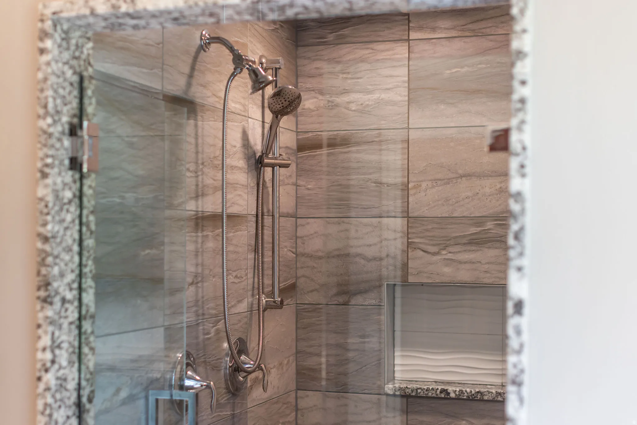 Glass-enclosed shower with a brushed nickel shower system, full-height tile surround, built-in niche, and granite-finish threshold
