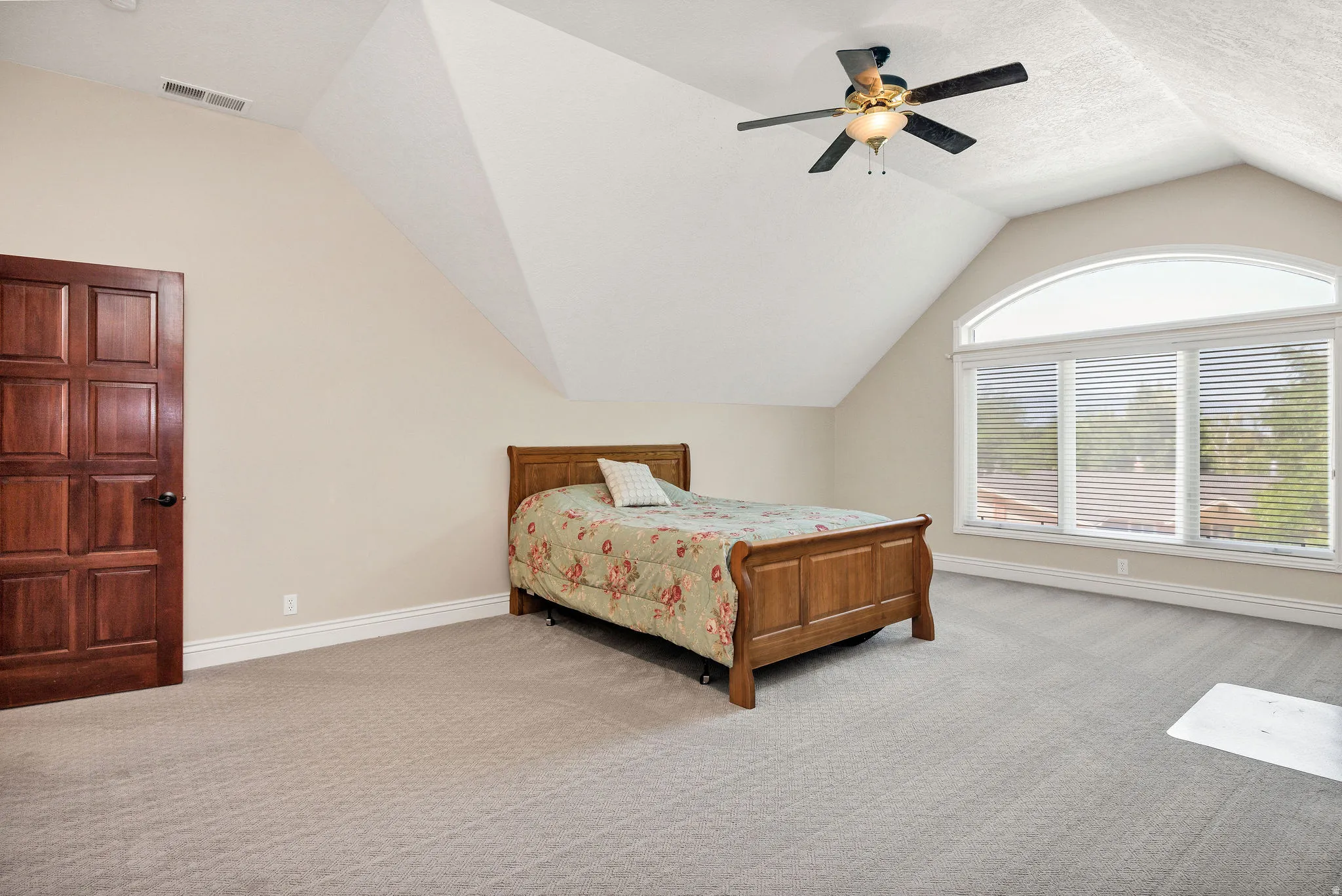 Vaulted ceiling with ceiling fan, arched window with horizontal blinds, neutral carpet, and paneled wood door
