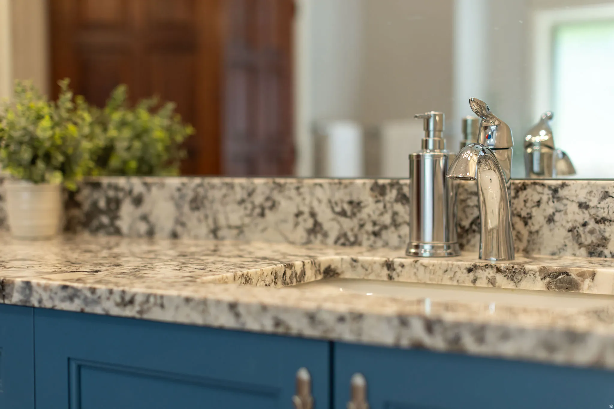 Undermount sink with a chrome faucet, set into a granite countertop and a blue vanity