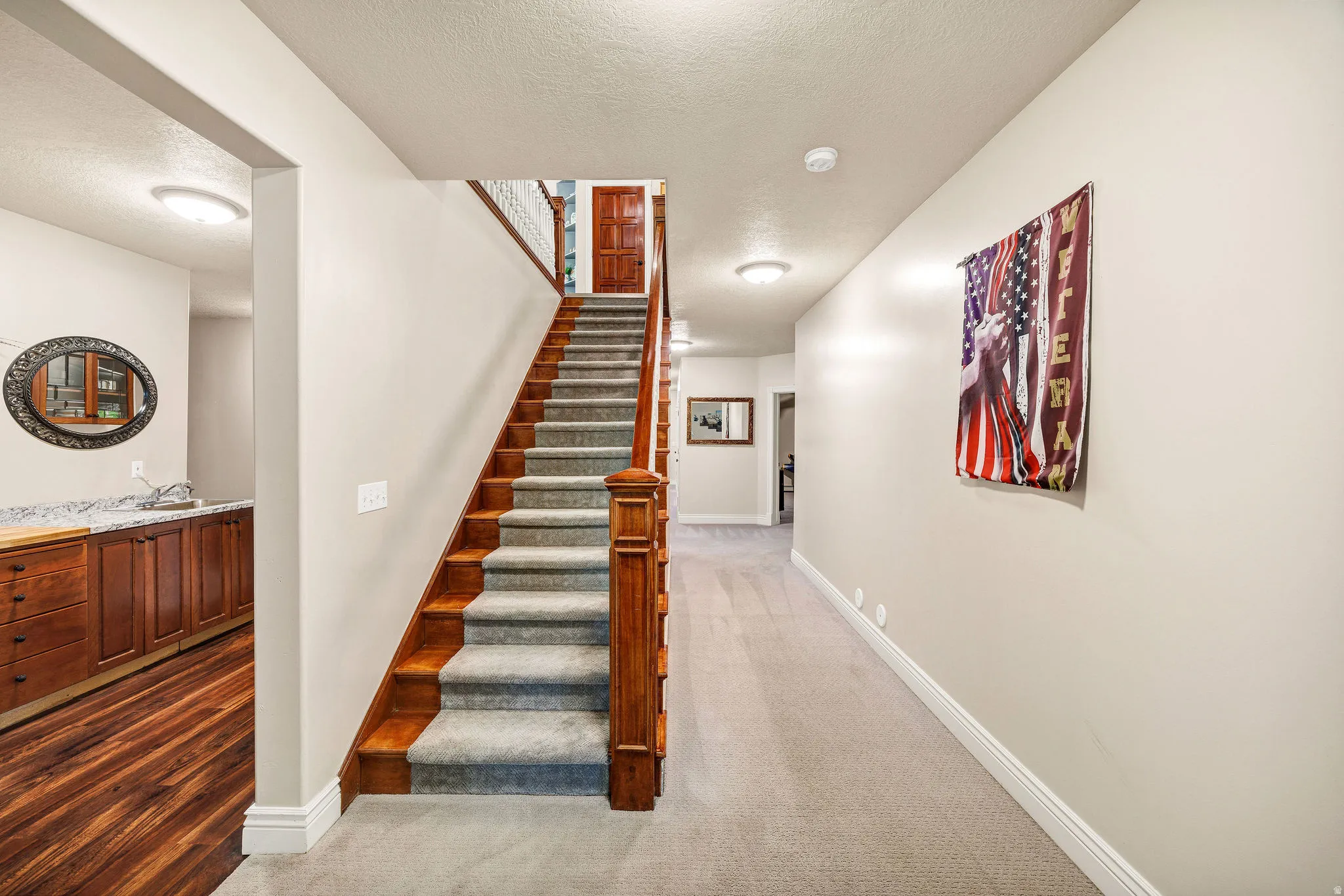 Wood-finish flooring, built-in cabinetry with a light-toned countertop, carpeted hallway, wood-finish staircase with carpeted treads, and recessed lighting
